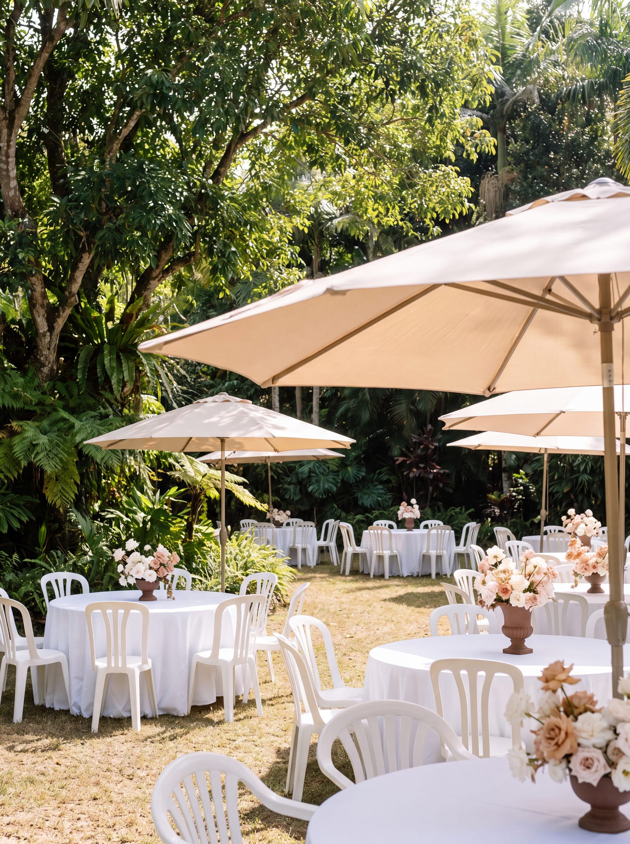 Ombrelones bege abertos sobre mesas redondas de uma recepção em um jardim tropical
